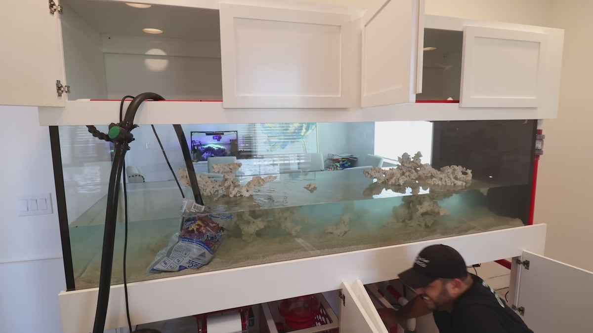 Built-in aquarium framed by custom cabinetry being filled and plumbed during installation